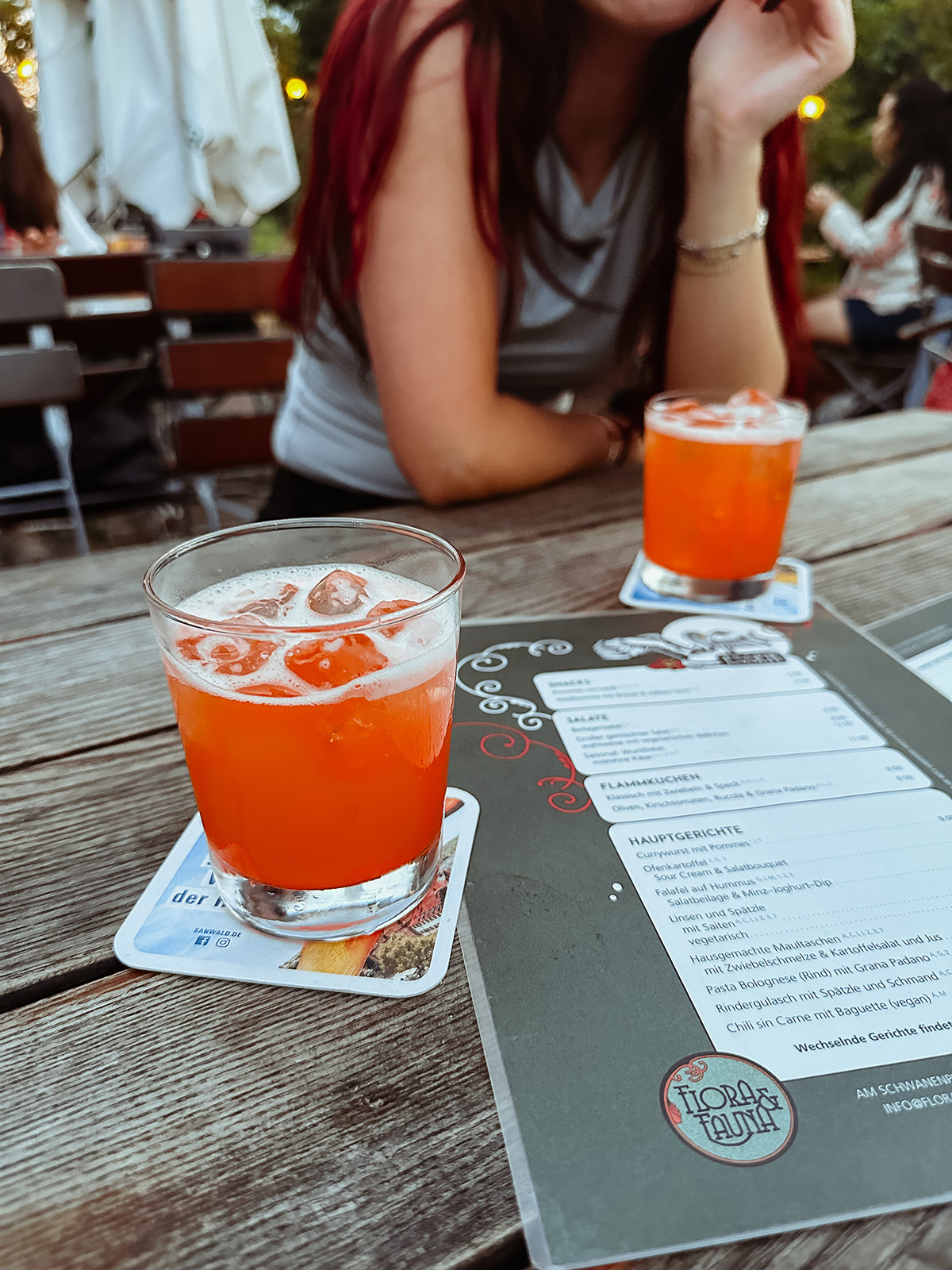 zwei orangefarbene Drinks in tiefen Gläsern auf einem Holztisch auf der Terrasse im Flora und Fauna in Stuttgart