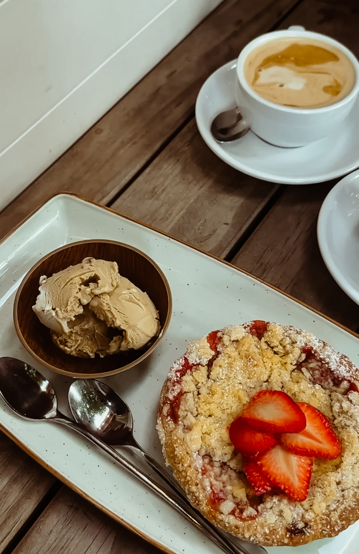 ein Erdbeercrumble-Törtchen neben einer Kugel hellbraunem Eis auf einem Teller im Café Gottlieb in Bad Cannstatt, dazu ein kaffeee auf einem Holztisch