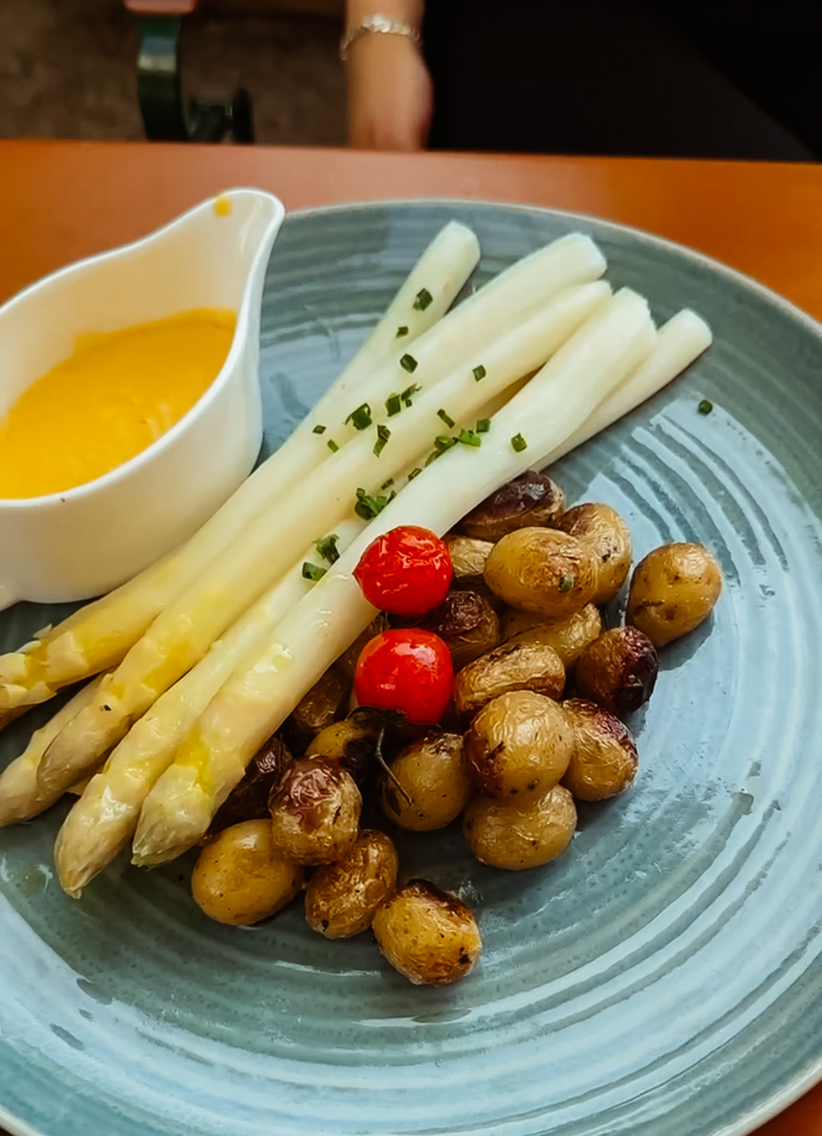 weißer Spargel mit einem Kännchen Sauce Hollandaise und Rosmarinkartoffeln mit zwei gegrillten Cherrytomaten auf einem türkisen Teller im Restaurant Kursaal in Stuttgart