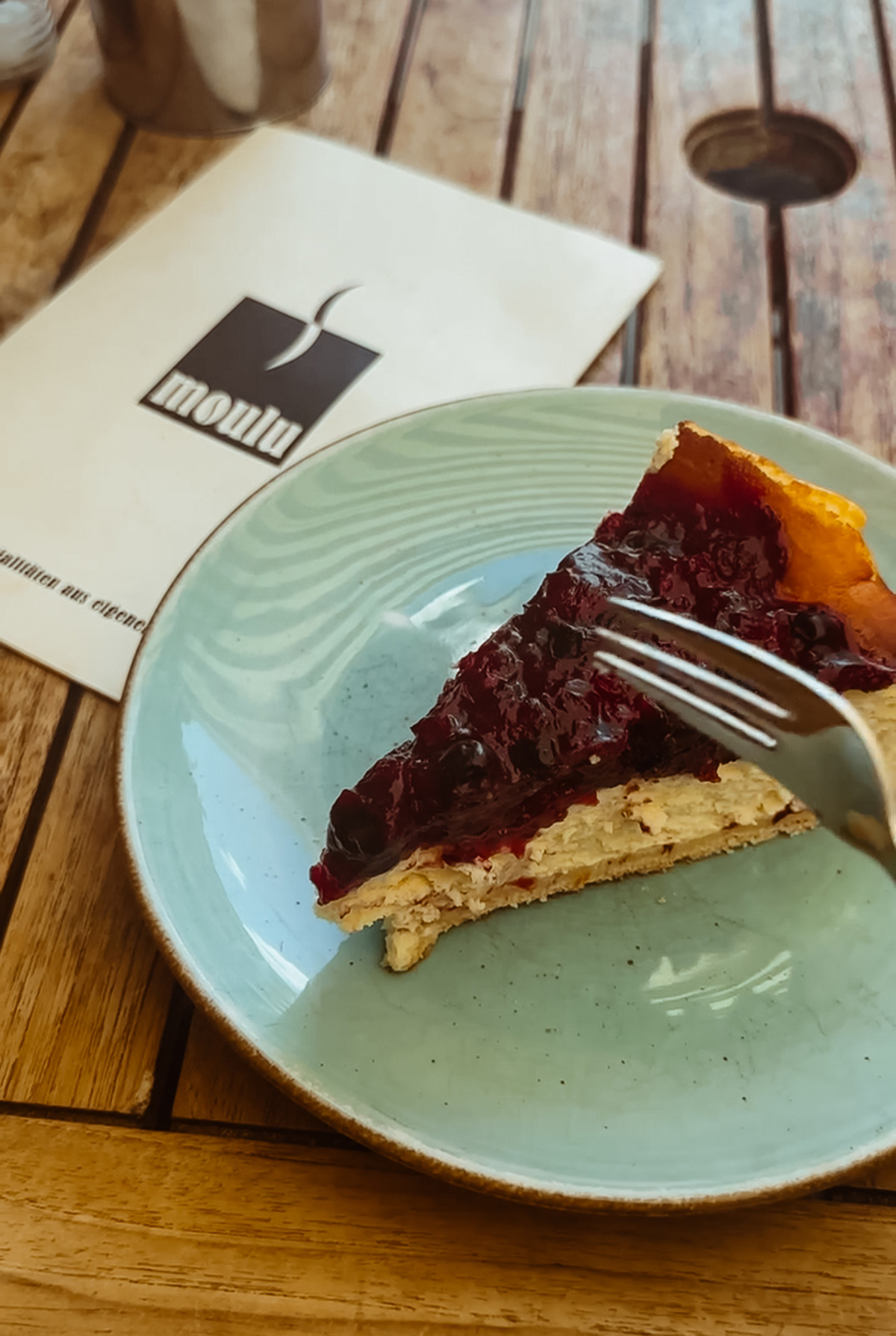 ein Stück Kuchen mit Beeren und heller Creme auf einem türkisen Teller neben einer Serviette mit dem Aufdruck Moulou im Café Moulu in Stuttgart-West