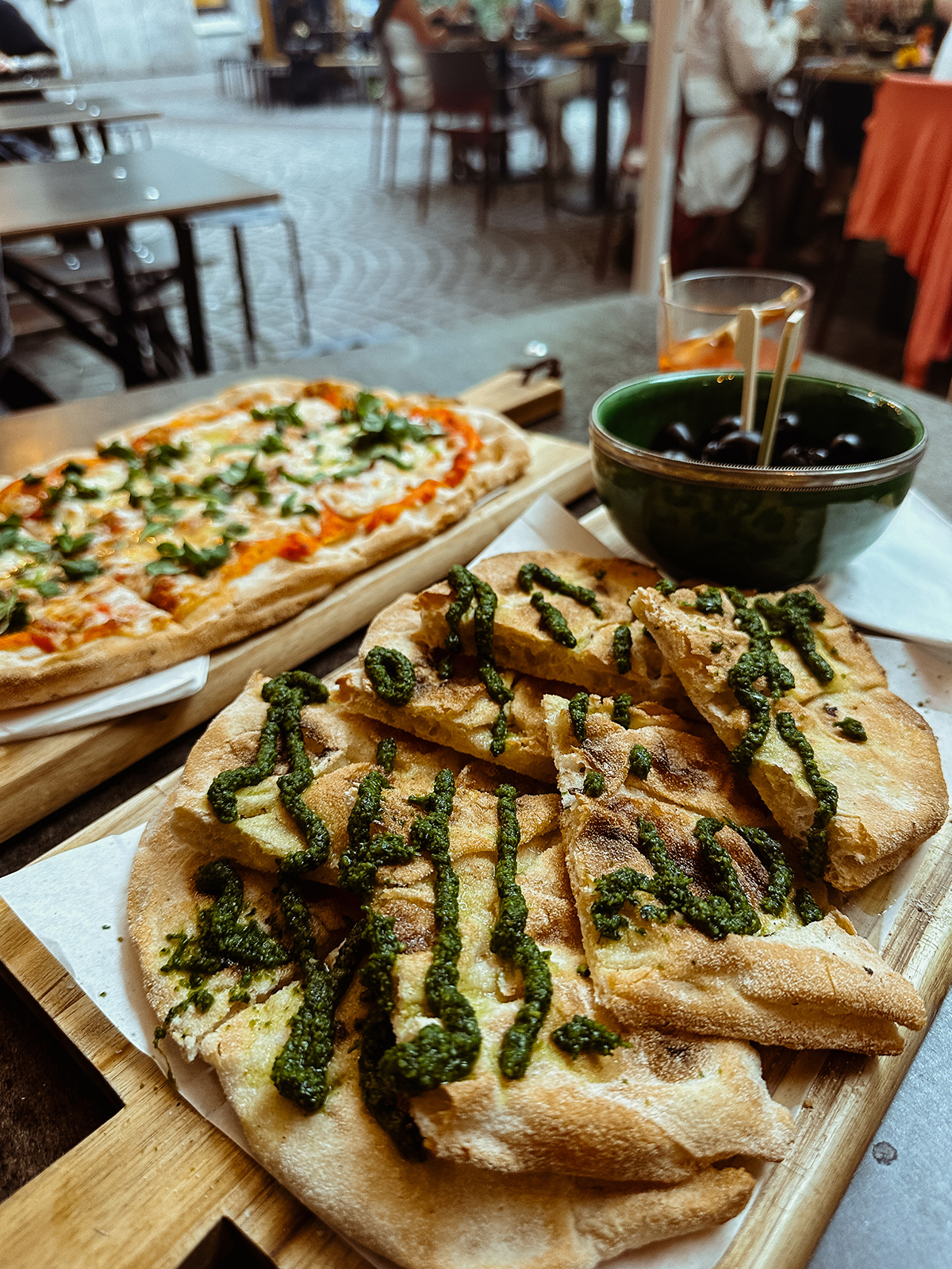 Pinsa mit Pesto sowie mit pizza-ähnlichem Belag und einer Schale Oliven auf dem Tisch der White Noise Bar in Stuttgart