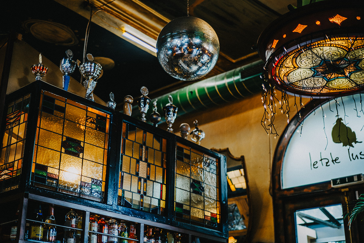 Diskokugel hängt von der Decke in der Letzten Instanz, während dahinter Pokale auf einer Bar platziert sind, welche mit Spirituosen befüllt ist