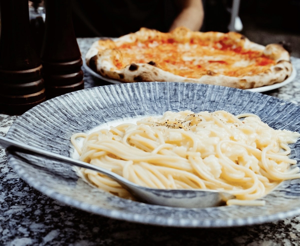 Ein Teller mit Spaghetti und ein Teller mit Pizza stehen auf dem Tisch. Daneben befinden sich ein Salz- und ein Pfefferstreuer.