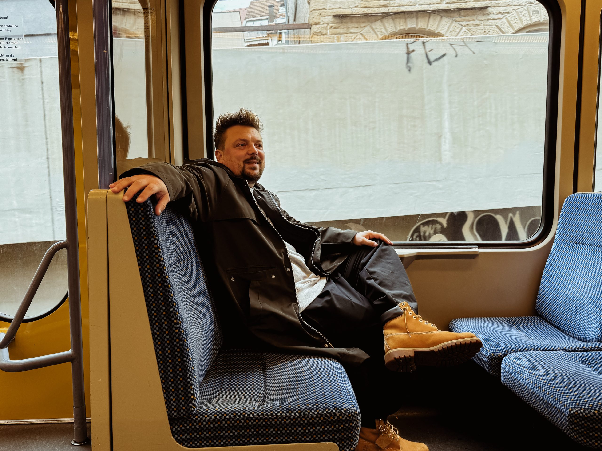 Bartek sitzt in der U-Bahn, hat eine Hand lässig auf den Sitz abgelegt und schaut aus dem Fenster