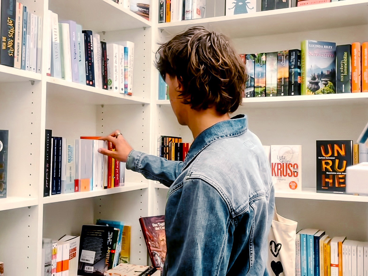 Ein junger Mann mit brauner Kurzhaarfrisur stöbern durch das Buch-Sortiment in den Regalen bei Schöne Dinge unweit der Haltestelle Neuer Markt in Leinfelden